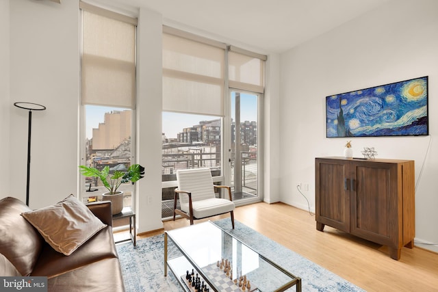 living room featuring light wood-style flooring, baseboards, a wall of windows, and a city view