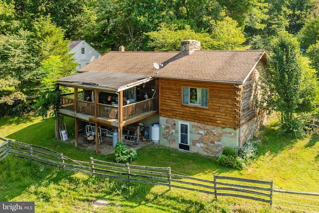 rear view of house with a chimney, a shingled roof, a lawn, log exterior, and a wooden deck