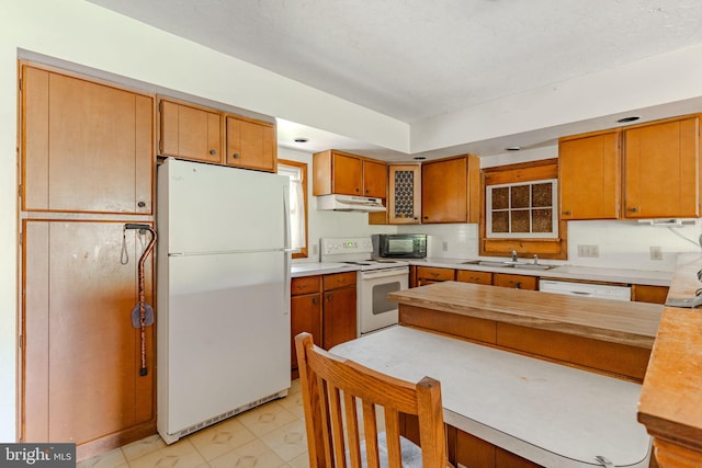 kitchen featuring brown cabinets, white appliances, a sink, and under cabinet range hood