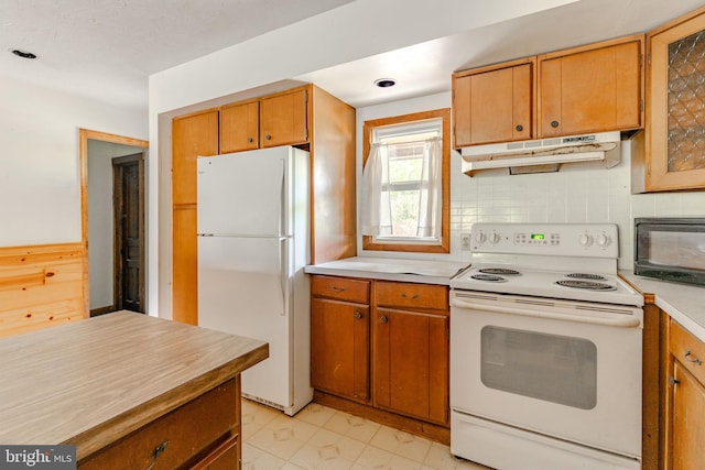 kitchen featuring white appliances, brown cabinets, light countertops, under cabinet range hood, and backsplash