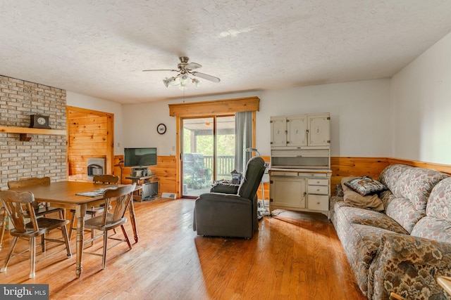 living room with light wood finished floors, wainscoting, wood walls, ceiling fan, and a textured ceiling