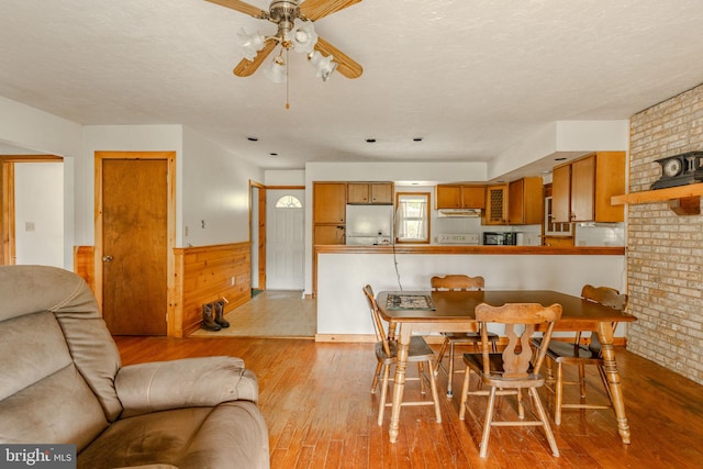 dining space with wainscoting, ceiling fan, a textured ceiling, and wood finished floors