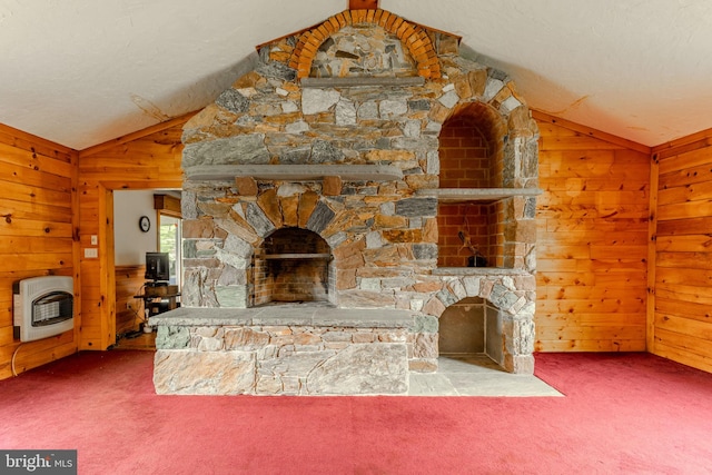 carpeted living room with heating unit, wooden walls, lofted ceiling, and a stone fireplace