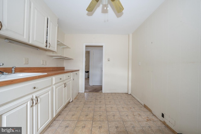 kitchen featuring light floors, light countertops, a ceiling fan, white cabinets, and a sink