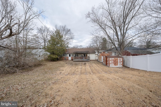 back of property featuring dirt driveway, a storage shed, fence, an outdoor structure, and a wooden deck