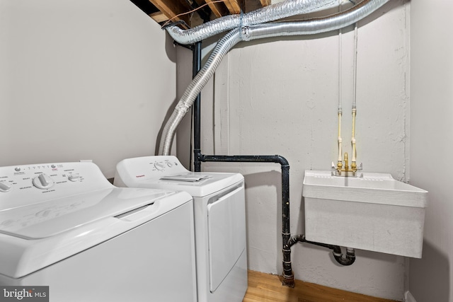 clothes washing area with a sink, laundry area, washer and dryer, and wood finished floors