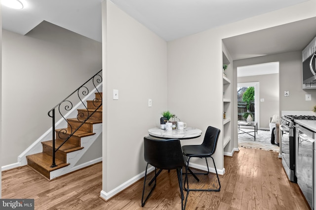 dining room featuring built in shelves, stairway, baseboards, and wood finished floors