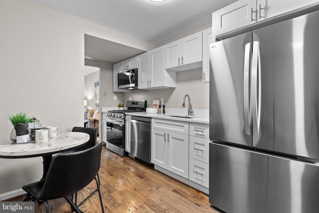 kitchen with wood finished floors, a sink, white cabinets, light countertops, and appliances with stainless steel finishes