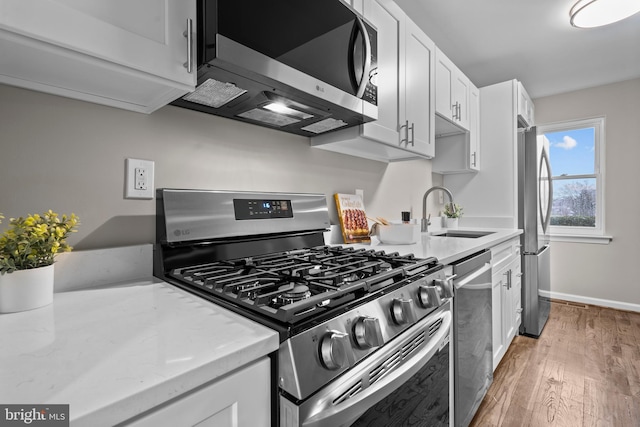 kitchen featuring white cabinets, light stone countertops, stainless steel appliances, light wood-type flooring, and a sink