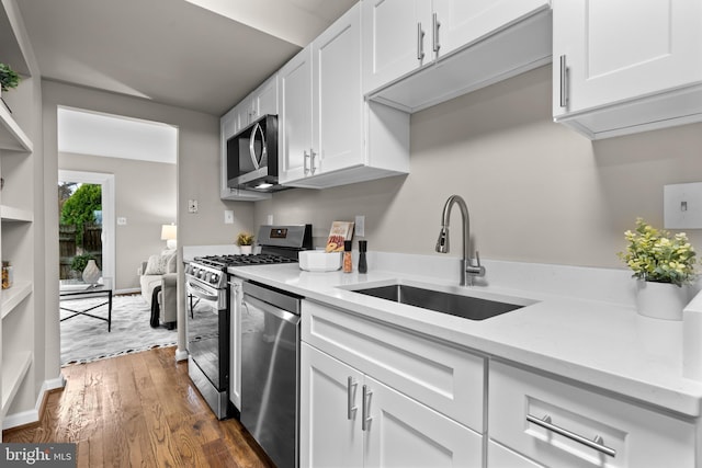 kitchen with stainless steel appliances, a sink, white cabinets, light countertops, and dark wood finished floors