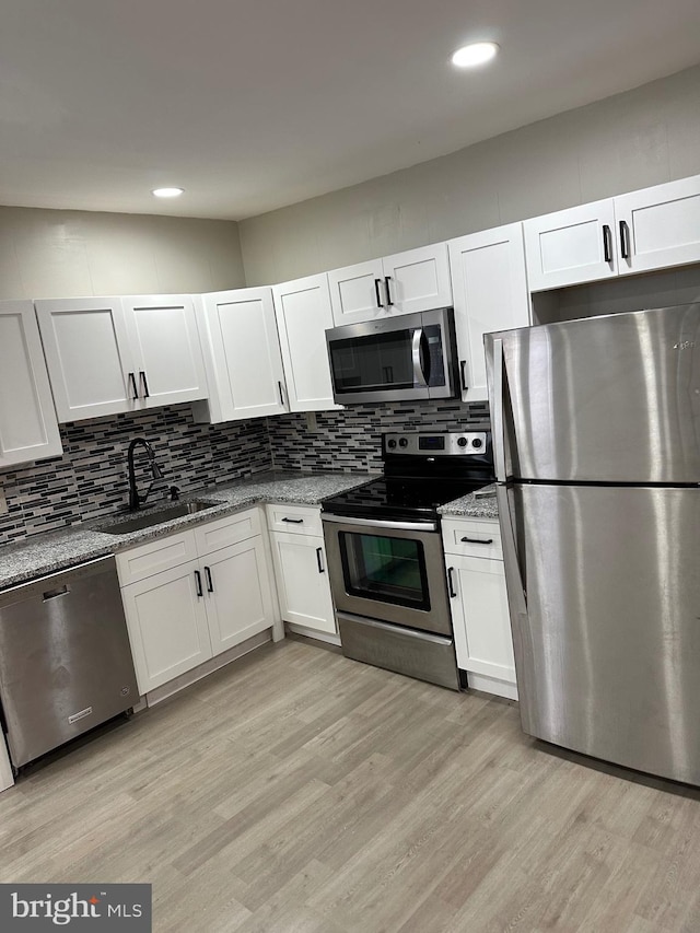 kitchen with decorative backsplash, light stone countertops, stainless steel appliances, light wood-style floors, and a sink