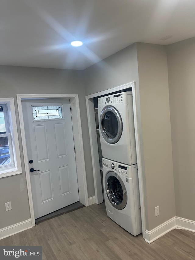 clothes washing area featuring laundry area, wood finished floors, stacked washer and clothes dryer, and baseboards