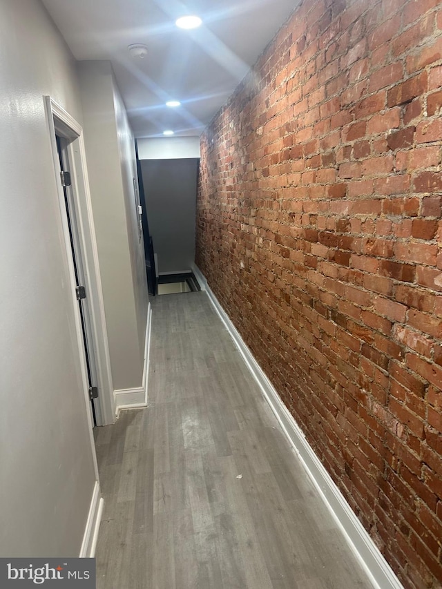 hallway with brick wall, wood finished floors, and baseboards