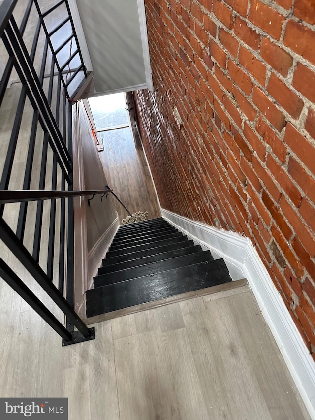 stairway with brick wall, wood finished floors, and baseboards