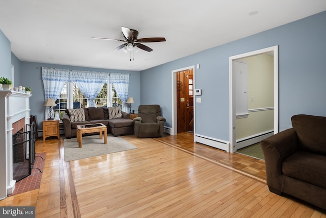 living room with a baseboard radiator, a baseboard heating unit, a fireplace with flush hearth, a ceiling fan, and light wood-style floors