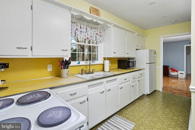 kitchen featuring electric range oven, freestanding refrigerator, light countertops, white cabinetry, and a sink