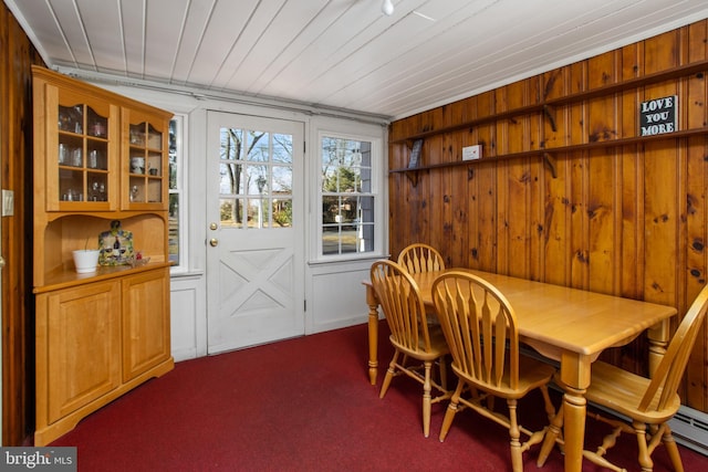 dining area featuring dark colored carpet, baseboard heating, wooden ceiling, and wooden walls