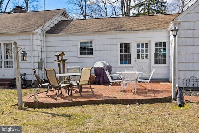 rear view of property featuring a patio area, a shingled roof, a chimney, and a lawn