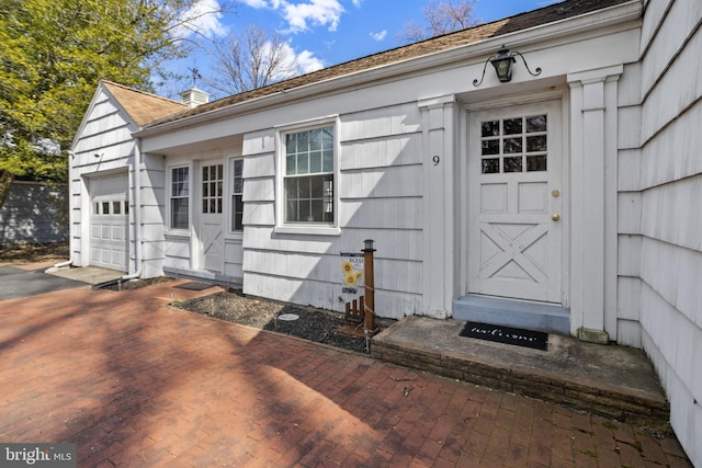 view of exterior entry featuring a garage, decorative driveway, and a chimney