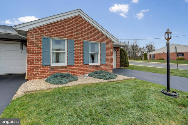 view of side of property with brick siding, a garage, driveway, and a yard