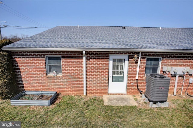 back of house with central air condition unit, brick siding, roof with shingles, and a lawn