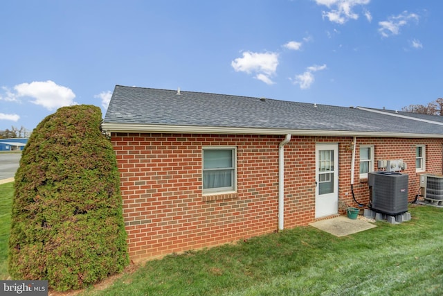 rear view of property with brick siding, a lawn, central AC, and roof with shingles