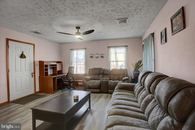 living room featuring a textured ceiling, ceiling fan, visible vents, and light wood-type flooring