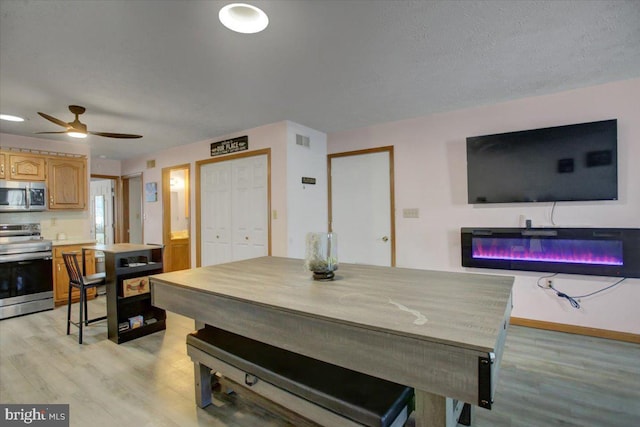 dining space with visible vents, ceiling fan, baseboards, light wood-style floors, and a glass covered fireplace