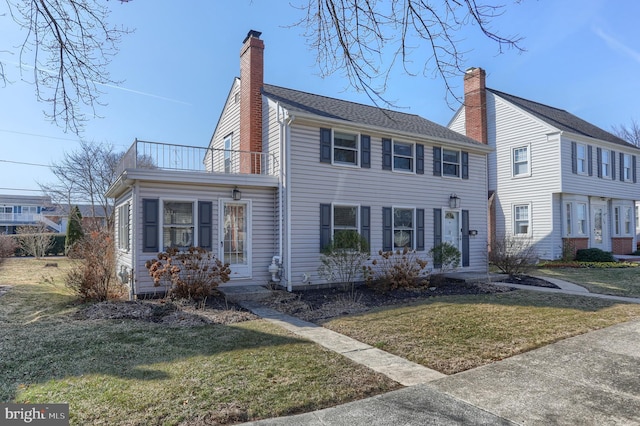 view of front of house with a chimney, a front lawn, and a balcony