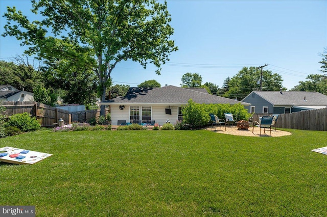 rear view of house with a fenced backyard, a yard, and a fire pit