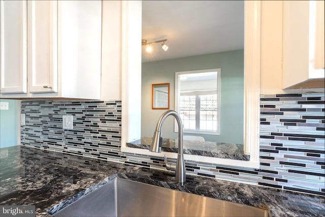 kitchen with dark stone counters, white cabinets, a sink, and decorative backsplash