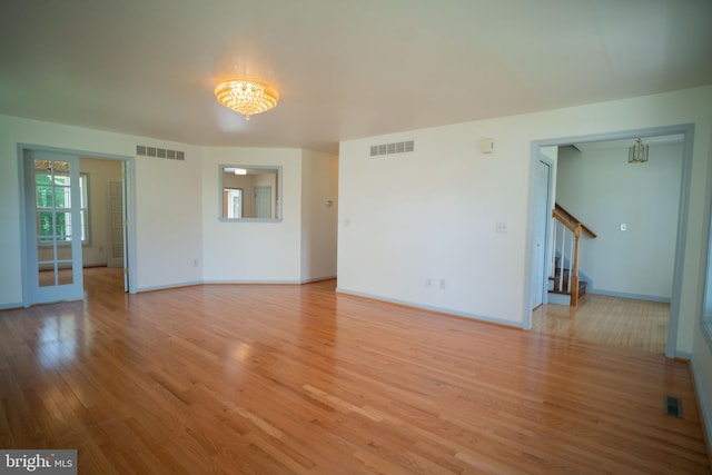 unfurnished living room featuring stairs, wood finished floors, visible vents, and a chandelier