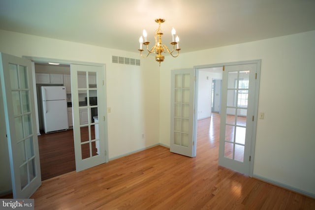 interior space with light wood finished floors, visible vents, a notable chandelier, and french doors