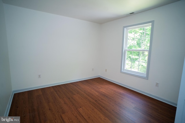 unfurnished room featuring plenty of natural light, visible vents, dark wood finished floors, and baseboards