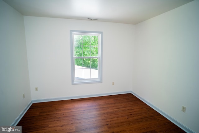 spare room featuring dark wood-style flooring, visible vents, and baseboards