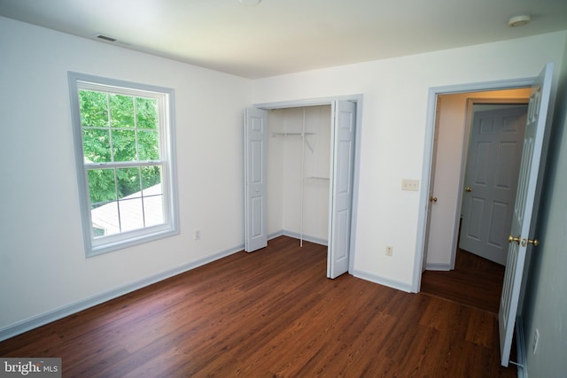 unfurnished bedroom with dark wood-type flooring, a closet, visible vents, and baseboards