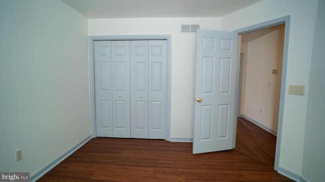 unfurnished bedroom with dark wood-style floors, a closet, visible vents, and baseboards