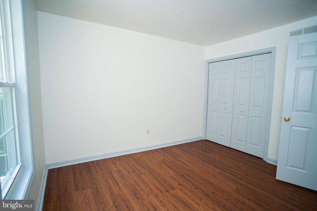 unfurnished bedroom featuring multiple windows, dark wood finished floors, and baseboards