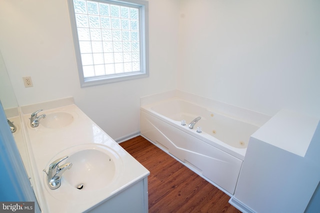 full bathroom with double vanity, wood finished floors, a jetted tub, and a sink