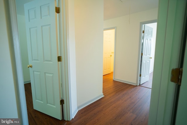 corridor featuring attic access, baseboards, and dark wood-style flooring