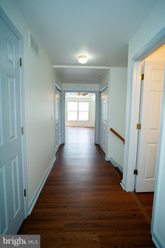 hallway with baseboards, visible vents, dark wood finished floors, and an upstairs landing