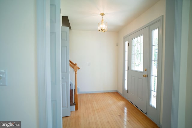 foyer entrance with light wood-style floors, baseboards, stairway, and an inviting chandelier