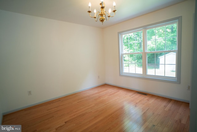 spare room with baseboards, light wood finished floors, visible vents, and an inviting chandelier