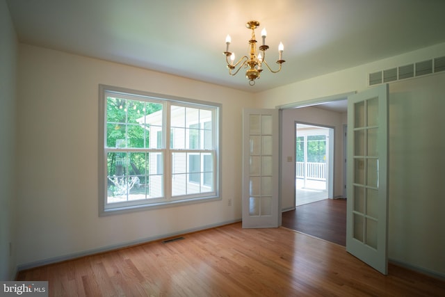 unfurnished dining area with french doors, visible vents, a notable chandelier, and wood finished floors