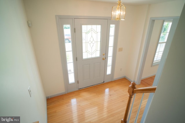 foyer entrance featuring light wood-type flooring, a notable chandelier, baseboards, and stairs