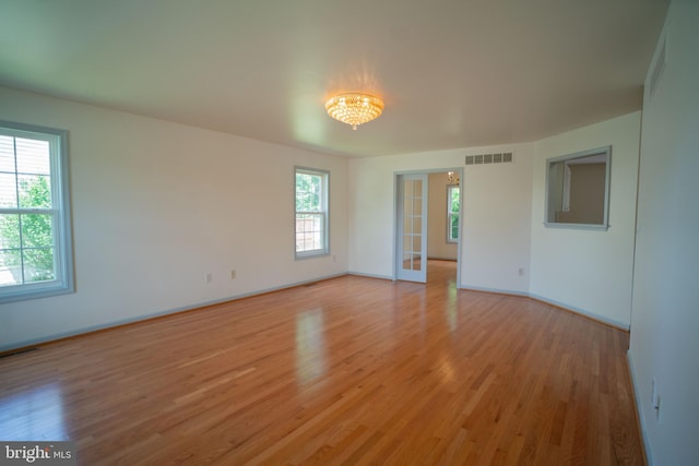 spare room featuring light wood-type flooring, baseboards, visible vents, and a chandelier