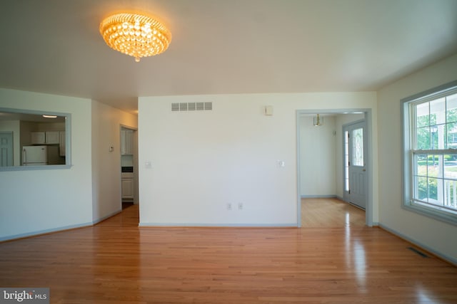 unfurnished living room featuring light wood-type flooring, visible vents, and a notable chandelier