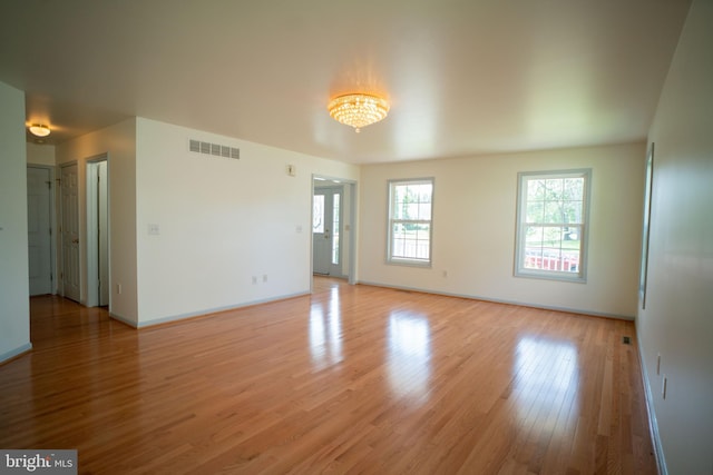 empty room featuring an inviting chandelier, light wood-type flooring, visible vents, and baseboards