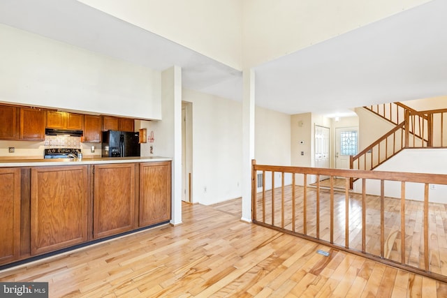 kitchen featuring black fridge with ice dispenser, brown cabinetry, light wood-type flooring, range, and under cabinet range hood