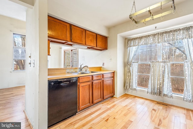 kitchen with visible vents, brown cabinetry, dishwasher, light wood-style floors, and a sink